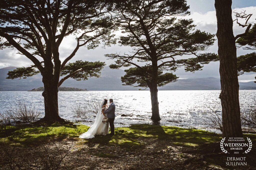 A bride and groom stand by the lakeside in the Killarney Golf and Fishing Club in Kerry, looking out towards the mountains
