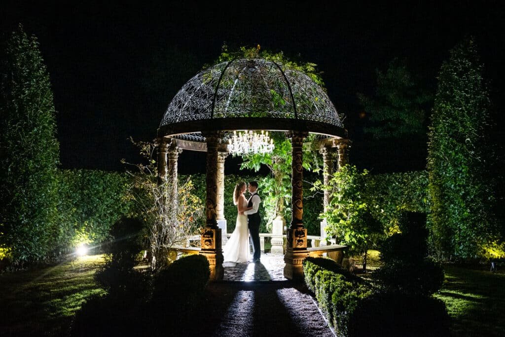 A bride and groom stand backlit at night by off camera flash in the temple in the gardens of Ballyseede Castle in Tralee, Ireland